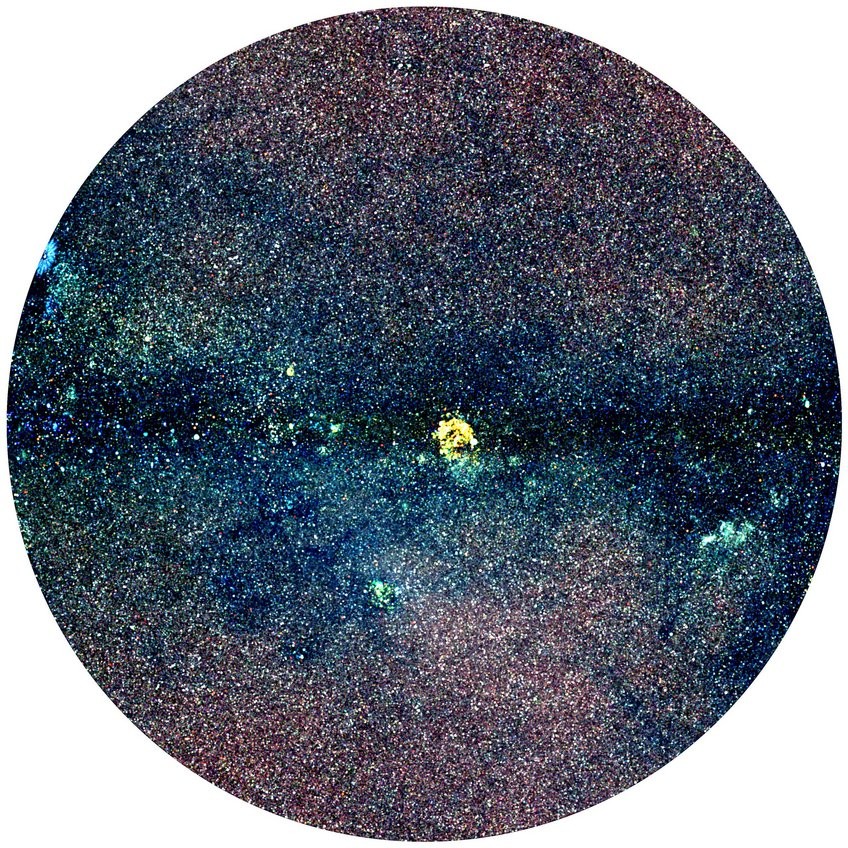 Circular astronomical image showing a dense distribution of stars across the field with a distinct bright yellow cluster near the middle, highlighting stellar concentration.